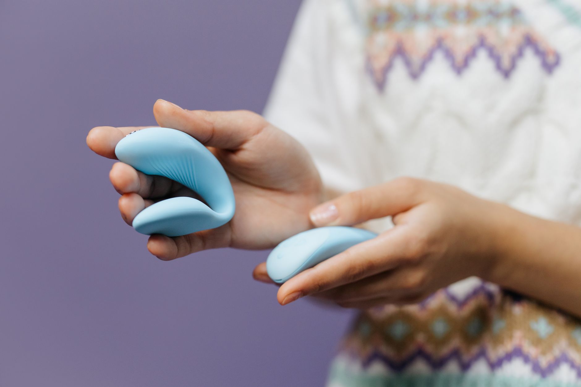 Two hands holding pink and blue silicone vibrators together on a pastel background, symbolizing couple reconnection