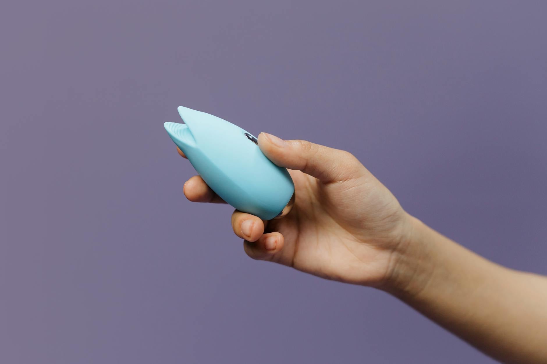 A blue silicone clitoral vibrator held in hand, representing modern self-pleasure and sensation exploration