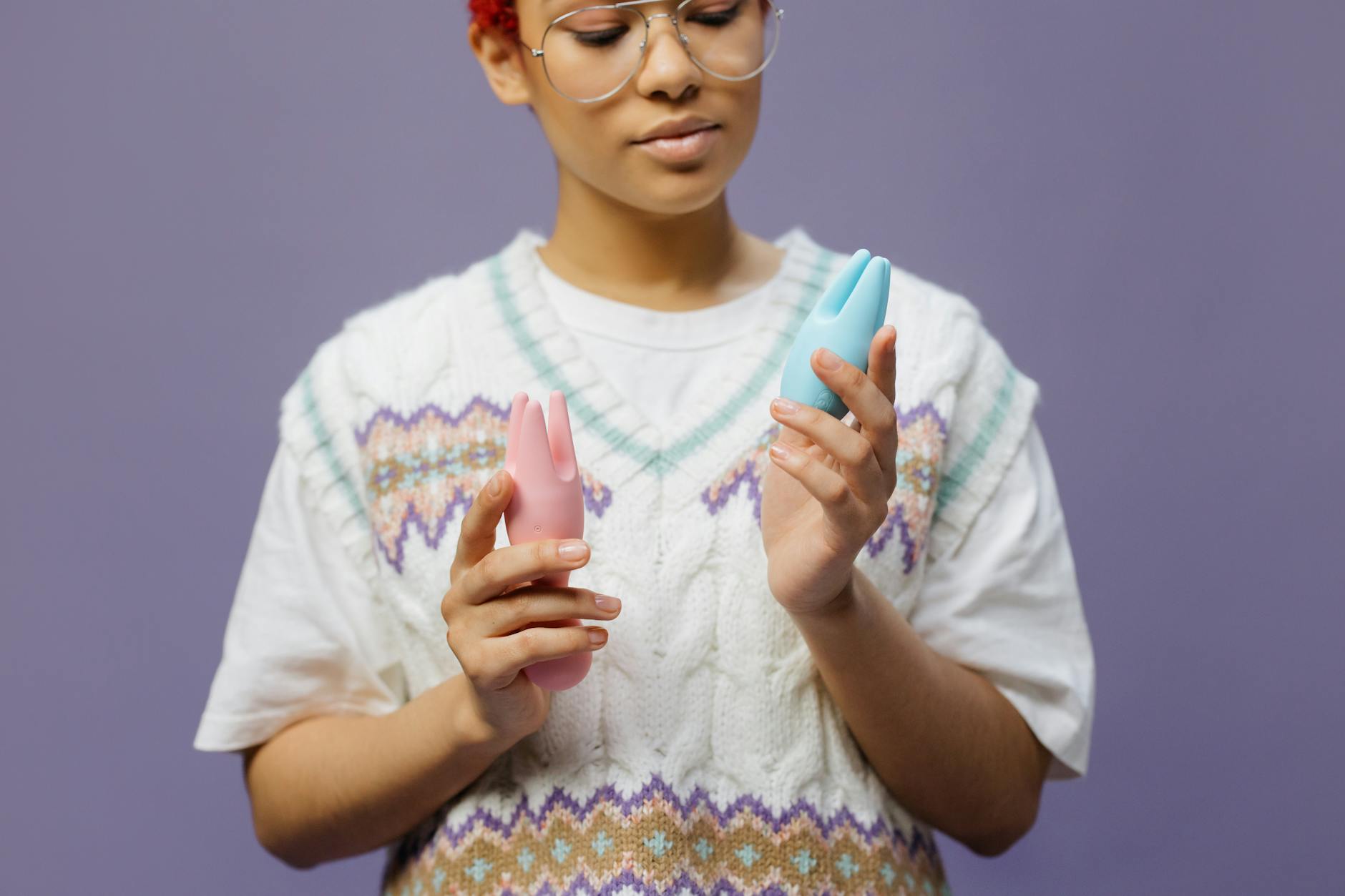 Woman holding pink and blue silicone vibrators thoughtfully, symbolizing gentle return to pleasure